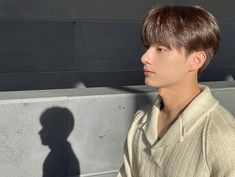 a young man standing next to a cement wall with his shadow on the wall behind him