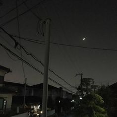 a street at night with power lines and telephone poles in the foreground, houses on either side