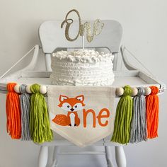 a white cake sitting on top of a table next to a wooden chair with an orange and green banner