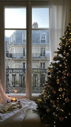 a christmas tree in front of a window with candles on the windowsill and a tray of food next to it