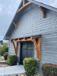 a gray house with wood trim and an arched window on the front door is surrounded by shrubbery