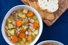 two bowls filled with soup next to bread on top of a cutting board and blue table cloth