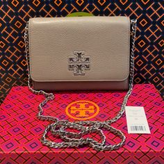 Nwt Auth Tory Burch Britten Chain Wallet Color Is French Gray Logo Is Hammered Silver Metal The Strap Has Leather Intertwined In The Metal Pebbled Leather Front Flap With Double Magnetic Snap Closure 1 Exterior Slip Pocket On Back 2 Interior Slip Pockets, 8 Card Slots, 1 Zip Pocket. Logo Lining Strap With (Approx.) 23" Drop Approximate Measurements 5.5" H X 7.5"L X 1.5" Silver Rectangular Wallet On Chain With Strap, Silver Leather Wallet On Chain With Chain Strap, Silver Rectangular Wallet On Chain For Everyday Use, Silver Wallet On Chain For Everyday Use, Elegant Silver Leather Wallet On Chain, Brown Leather Crossbody Purse, Tory Burch Crossbody Bag, Tory Burch Kira Chevron, Tory Burch Clutch