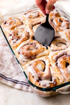 a person is spreading icing on top of cinnamon rolls in a glass baking dish