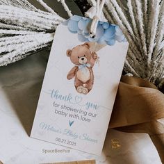 a baby shower tag with a teddy bear on it next to some flowers and branches