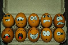 six eggs with different faces painted on them in an egg carton, all lined up and ready to be eaten