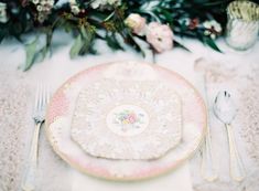 an elegant table setting with pink and white plates, silverware and floral centerpieces