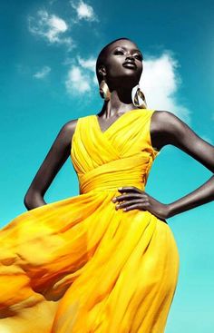 a woman in a yellow dress is standing with her hands on her hips and looking up at the sky