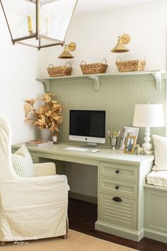 a desk with a computer on top of it next to a white chair and lamp