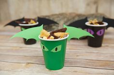 a green cup filled with cereal topped with toppings next to two black bat wings