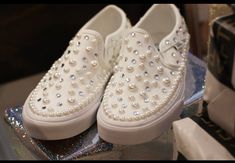 a pair of white shoes with pearls on them sitting on a table next to other items