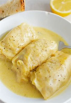 two pieces of fish are in a yellow sauce with bread on the side and lemon wedges