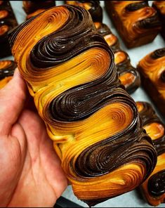 a hand is holding a piece of brown and yellow swirled pastry with chocolate icing on it