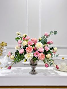 a vase filled with lots of pink and white flowers on top of a table next to a candle