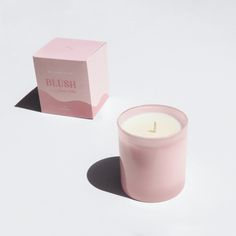 a pink candle sitting next to a box on a white surface with the word blush written in gold