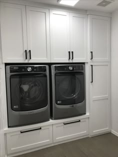 a washer and dryer in a white laundry room with built - in cabinets