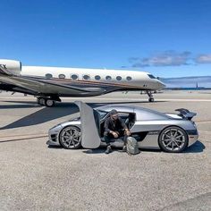 a man sitting in the driver's seat of a silver sports car next to an airplane