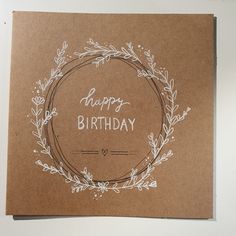 a brown card with a wreath and happy birthday written in white ink on it, sitting on top of a table