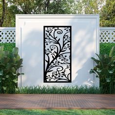 a white wall with a black metal design on it next to some grass and trees