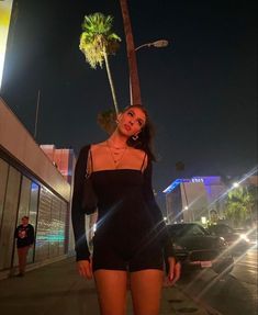 a woman is standing on the sidewalk in front of a palm tree