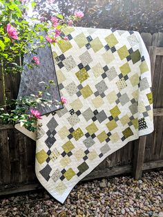 a quilt hanging on the side of a wooden fence next to a pink flower bush