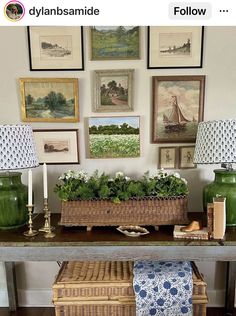 a table with two lamps and pictures on the wall above it, along with a basket filled with plants