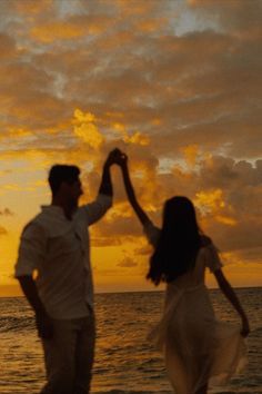 a man and woman dancing on the beach at sunset