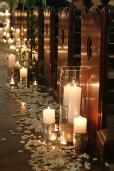 candles are lined up on the floor in front of pews with petals scattered around them