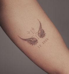 a woman's arm with a cross and wings tattoo on the left side of her arm