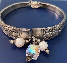 a close up of a silver bracelet on a blue surface with beads and charms around it