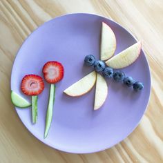 a purple plate topped with fruit and veggies on top of a wooden table