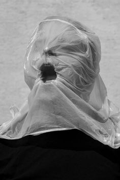 a black and white photo of a person with a plastic bag on their head looking at the water