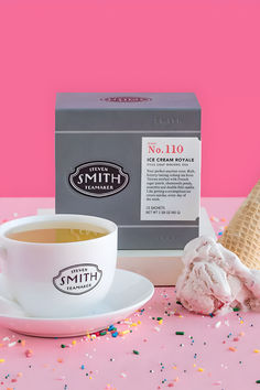 a cup of coffee next to an ice cream cone on a pink surface with sprinkles