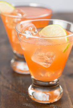 three glasses filled with orange liquid and limes on a wooden table, ready to be served