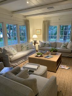 a living room with couches, chairs and tables in front of two large windows