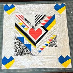 a white quilt with blue, yellow, and red designs on the top is laying on a table