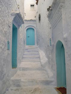 an alley way with white walls and blue doors