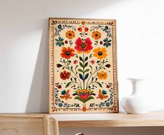 a white vase sitting on top of a wooden table next to a wall mounted art piece