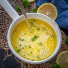 a white bowl filled with soup and garnished with parsley next to sliced lemons