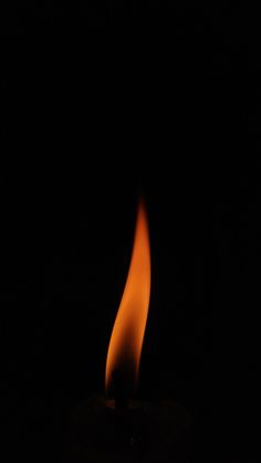 a lit candle in the dark with orange flames