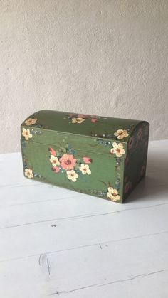 a green box with flowers on it sitting on a white table next to a wall