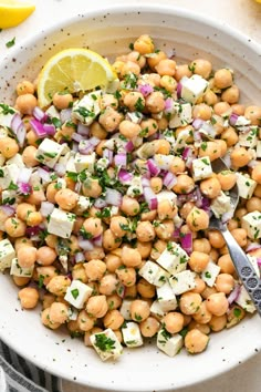 a white bowl filled with chickpeas, onions and feta cheese next to lemon wedges