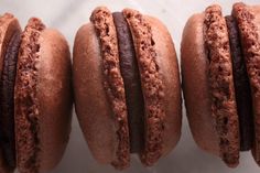 four chocolate macaroons are lined up on a white counter top and one is half eaten