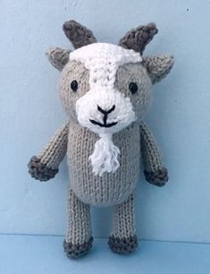 a knitted stuffed animal is posed against a blue wall, wearing a white and gray scarf