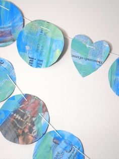 paper hearts are hanging from a string on a white wall with blue and green colors