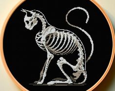 a cross - stitch skeleton cat is shown in an embroidery pattern on a black background