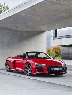 a red sports car parked in front of a concrete building with an overhang above it