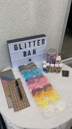 a white table topped with lots of crafting supplies next to a sign that says glitter bar