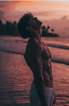 a man standing on top of a beach next to the ocean with his eyes closed