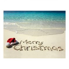 a merry christmas message written in the sand on a beach with santa's hat